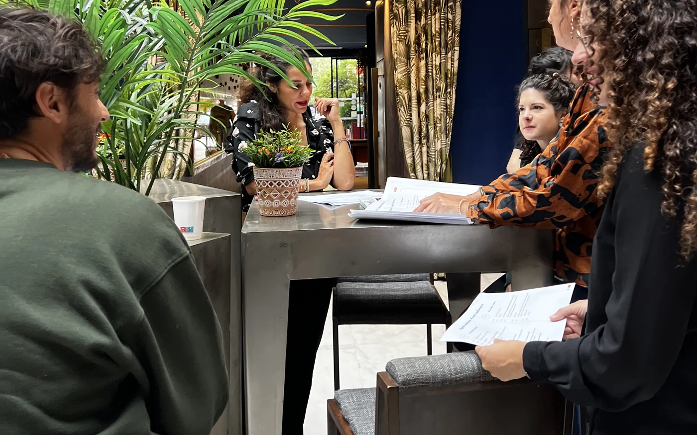 Participants au travail autour d'une table haute, documents en main, dans une salle éclairée par la lumière du jour